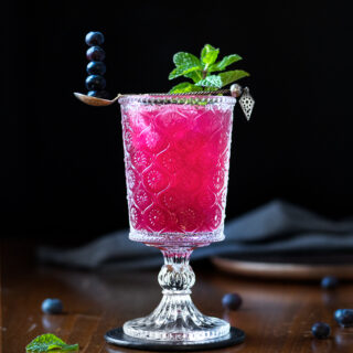 a bright pink cocktail with mint and a spoon of blueberries.