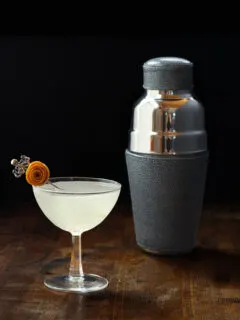 vintage coupe glass filled with a hazy liquid next to leather wrapped cocktail shaker.