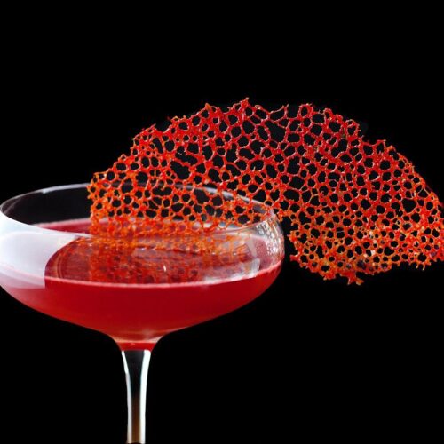 close up of a bright red coral tuile garnish on a red cocktail.