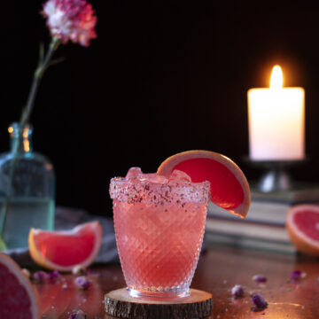 pink drink in a short glass with grapefruit wedge garnish next to a candle.