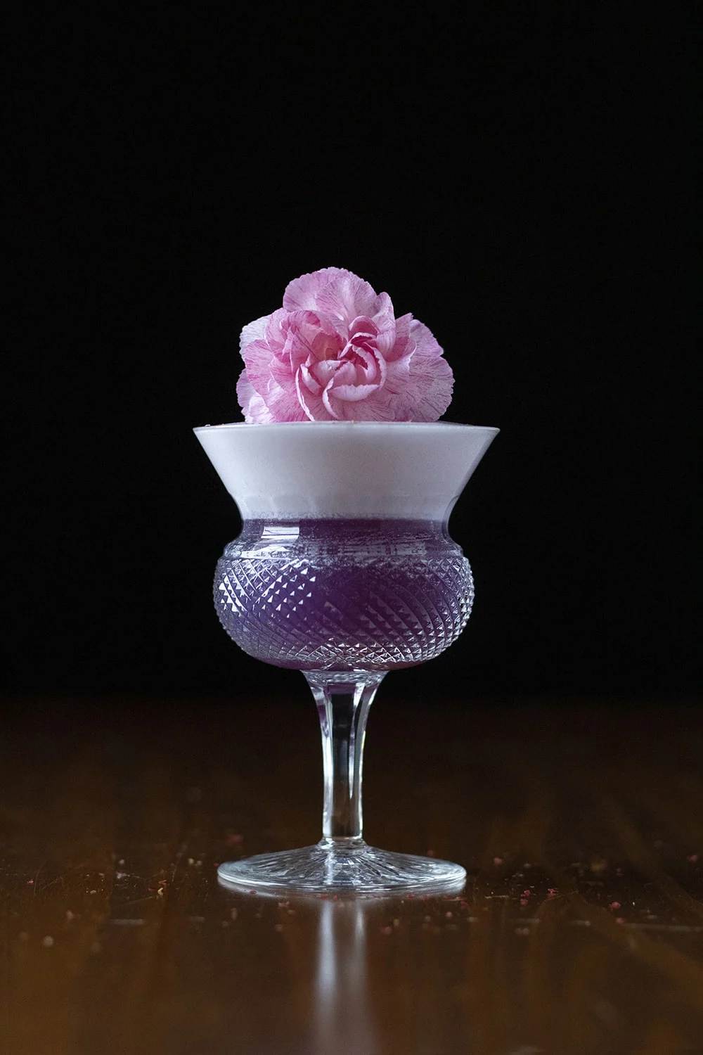 purple fancy cocktail with foam and pink floral garnish