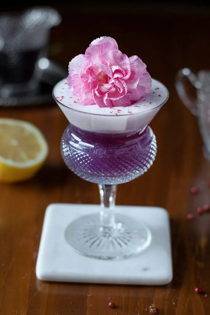 close up of purple cocktail with pink flower garnish.