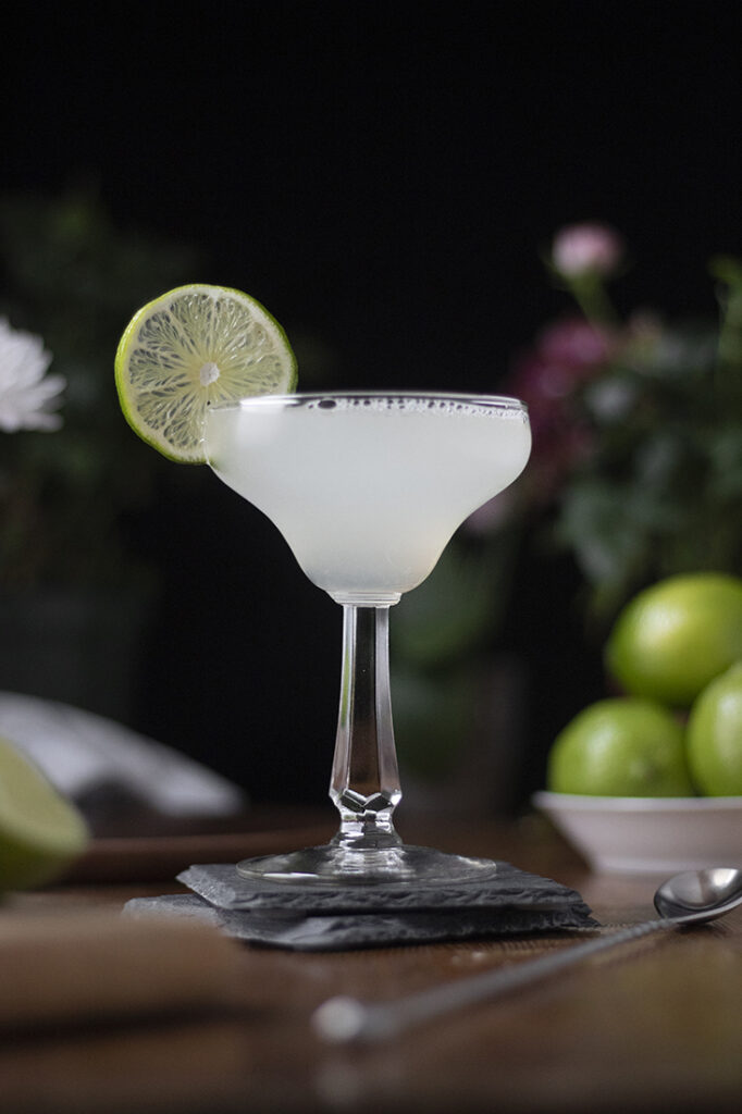 a cocktail in a vintage margarita glass with a lime wheel.