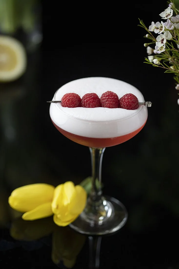 red cocktail with thick white foam on top and raspberries