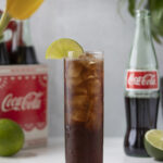 a tall glass of coca cola and ice garnished with a lime wheel.