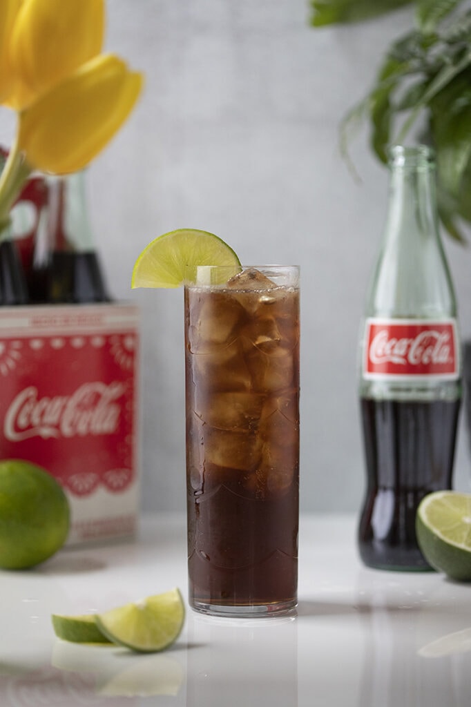 a tall glass of coca cola and ice garnished with a lime wheel.
