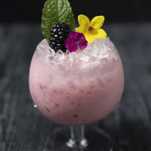 pink cocktail over crushed ice with edible flowers
