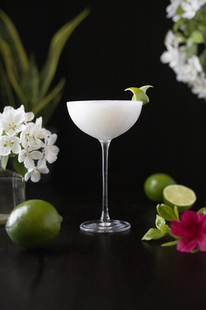 a white frozen drink in a long stemmed coupe glass with a lime twist.
