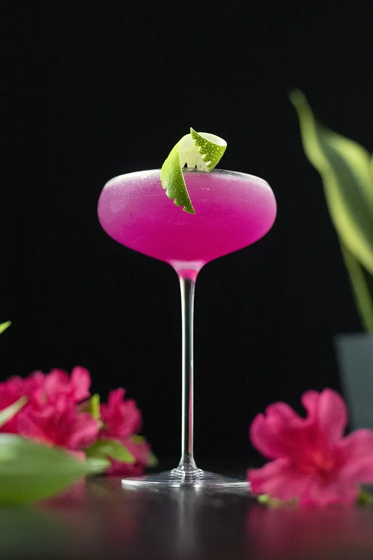 neon pink cocktail in a tall coupe glass with a lime twist