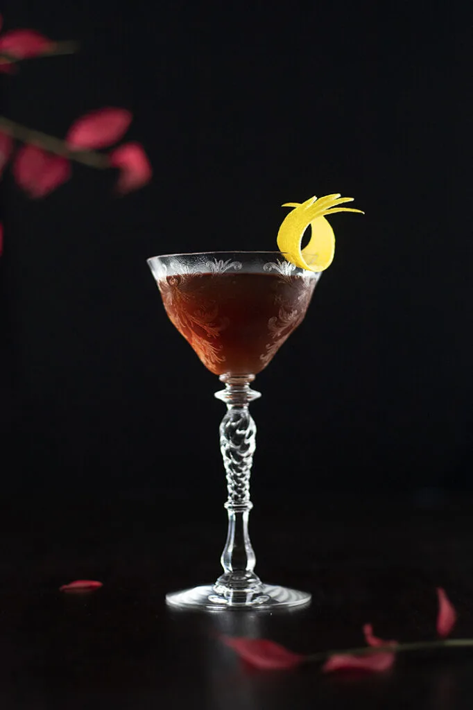 brown cocktail in a stemmed glass with a lemon twist