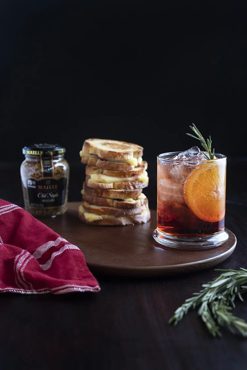 red cocktail on table with grilled cheese sandwich stack and jar of mustard