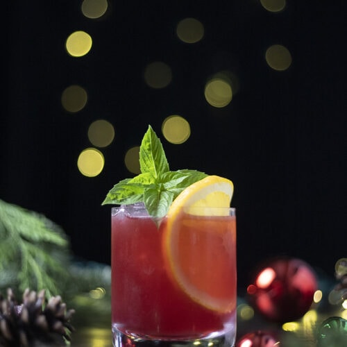 red drink garnished with basil and orange