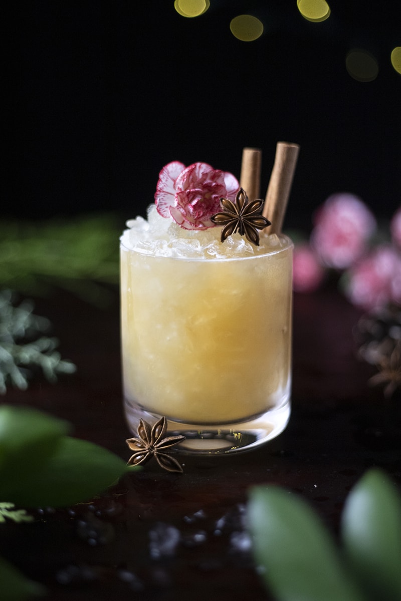 yellow cocktail in a rocks glass with crushed ice, star anise and cinnamon sticks