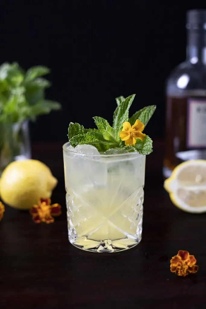 pale yellow cocktail in a rocks glass with mint and flowers