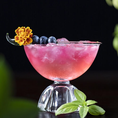 pink drink in a coupe glass with blueberries
