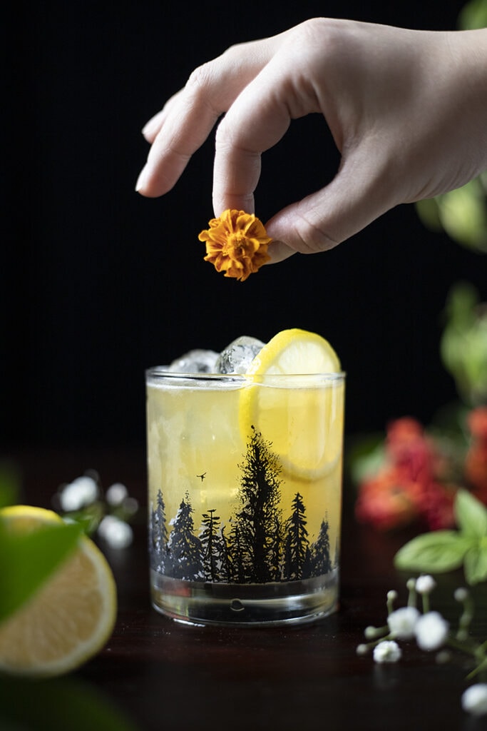 a hand adding an orange flower to a cocktail