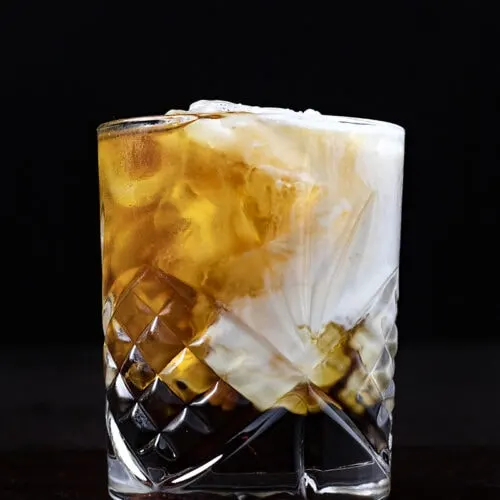 a rocks glass filled with swirling layers of white cream and brown liquors