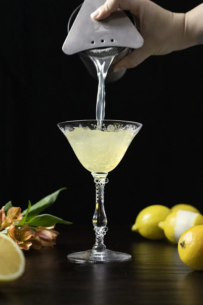 straining a cocktail into a vintage coupe glass