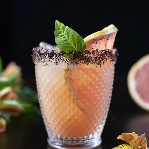 pink cocktail in a double rocks glass with grapefruit and a basil leaf