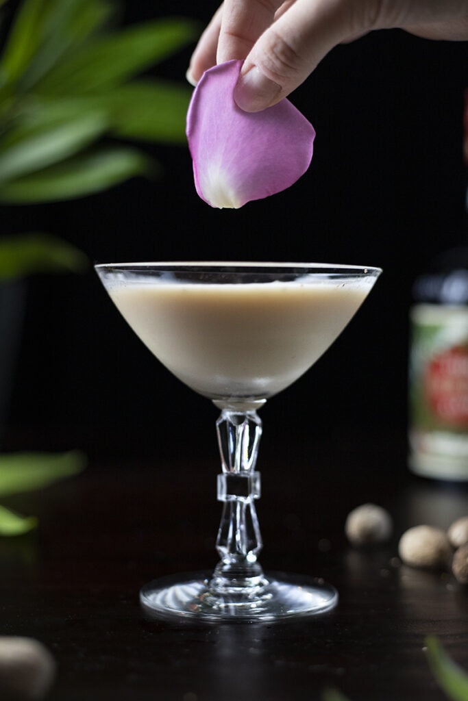 garnishing a cocktail with a pink rose petal