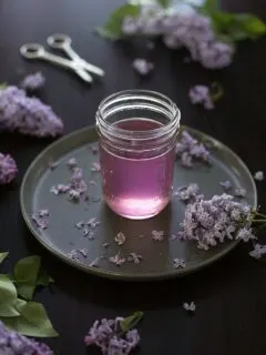 jar of purple liquid surrounded by lilac blossoms