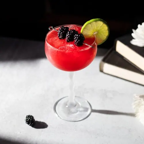 a bright red drink in a stemmed glass garnished with blackberries
