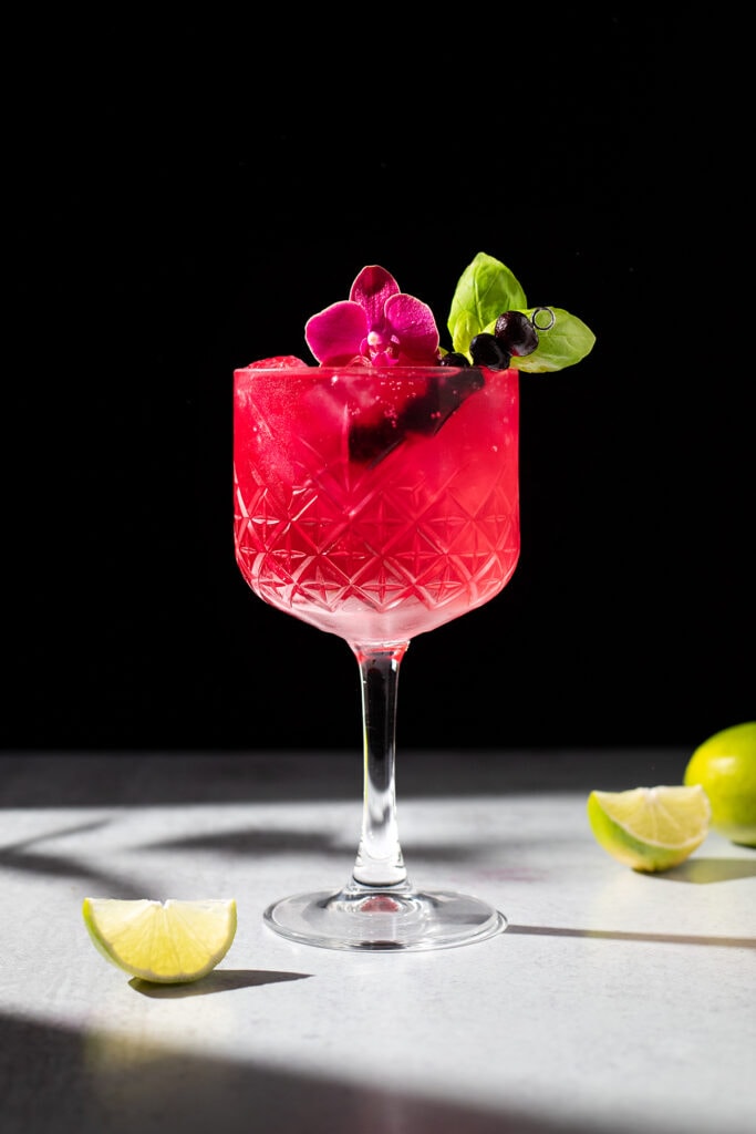 a bright pink drink in a stemmed glass with an orchid