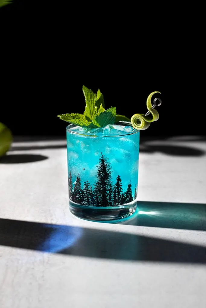 a blue drink with a sprig of mint and a fancy lime twist.