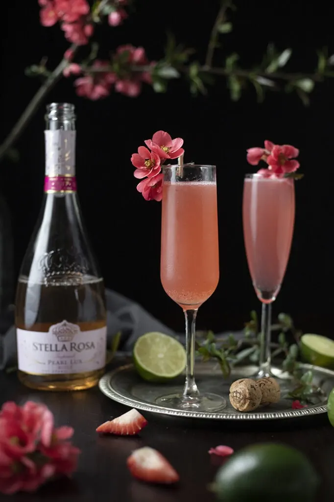two finished pink cocktails in champagne flutes garnished quince flowers