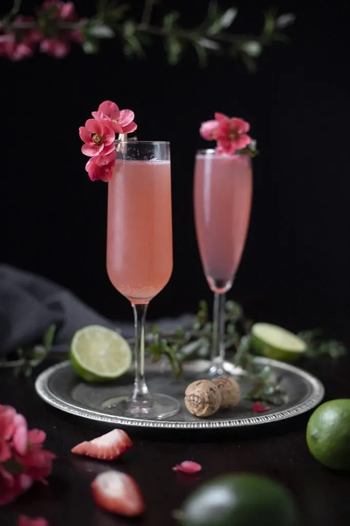 close up of two pink cocktails in champagne flutes garnished with pink quince blossoms