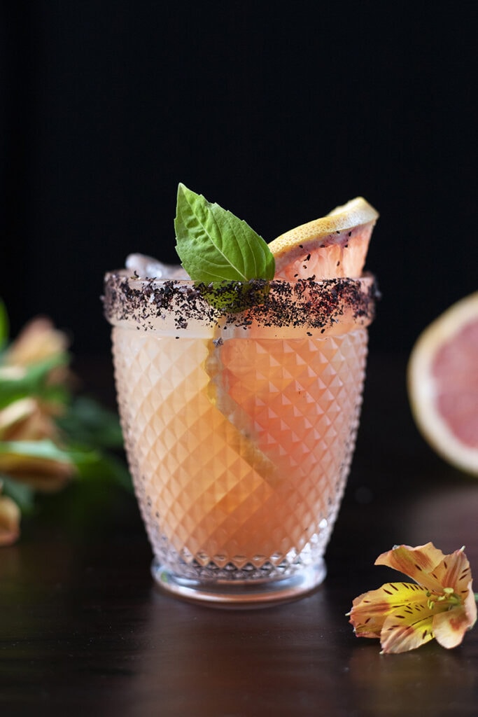 pink cocktail in a double rocks glass with grapefruit and a basil leaf