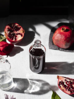 a small apothecary bottle with dark red liquid surrounded by pomegranates