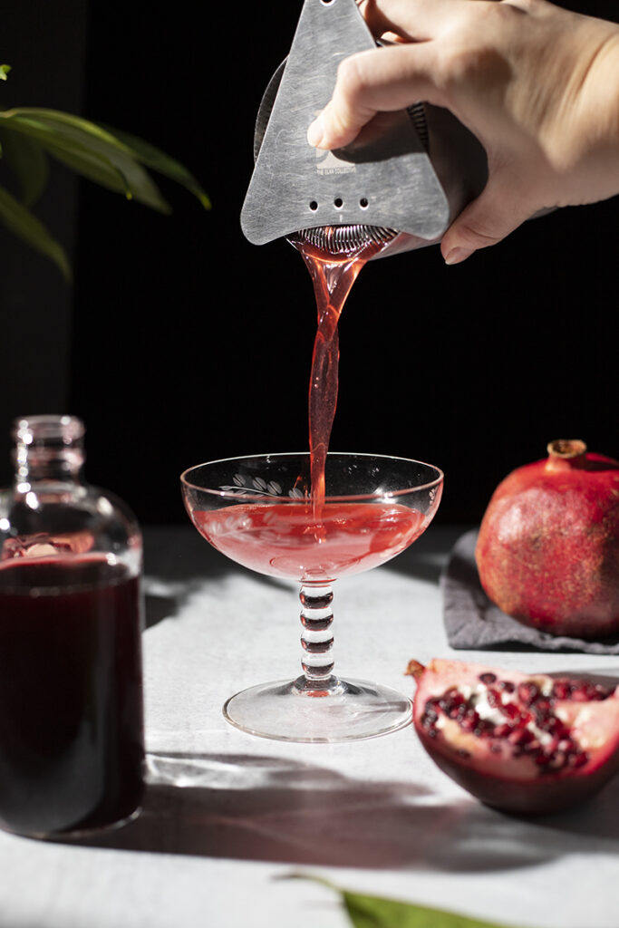 pouring a red cocktail into a coupe glass