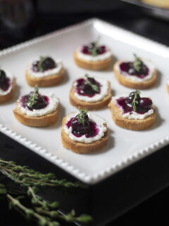a plate of small crostinis with goat cheese, blueberry compote and thyme