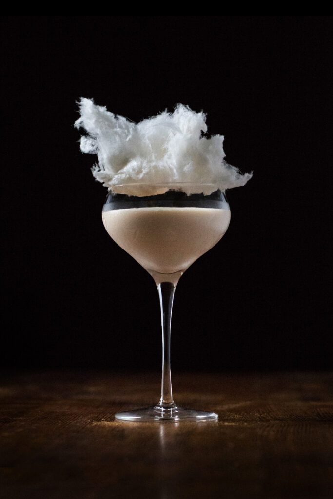 creamy cocktail in a coupe garnished with cotton candy.