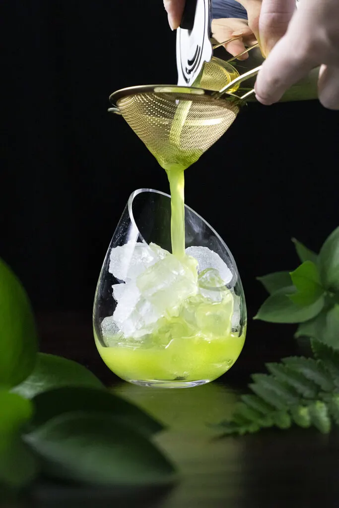 pouring a green drink through a fine mesh strainer.