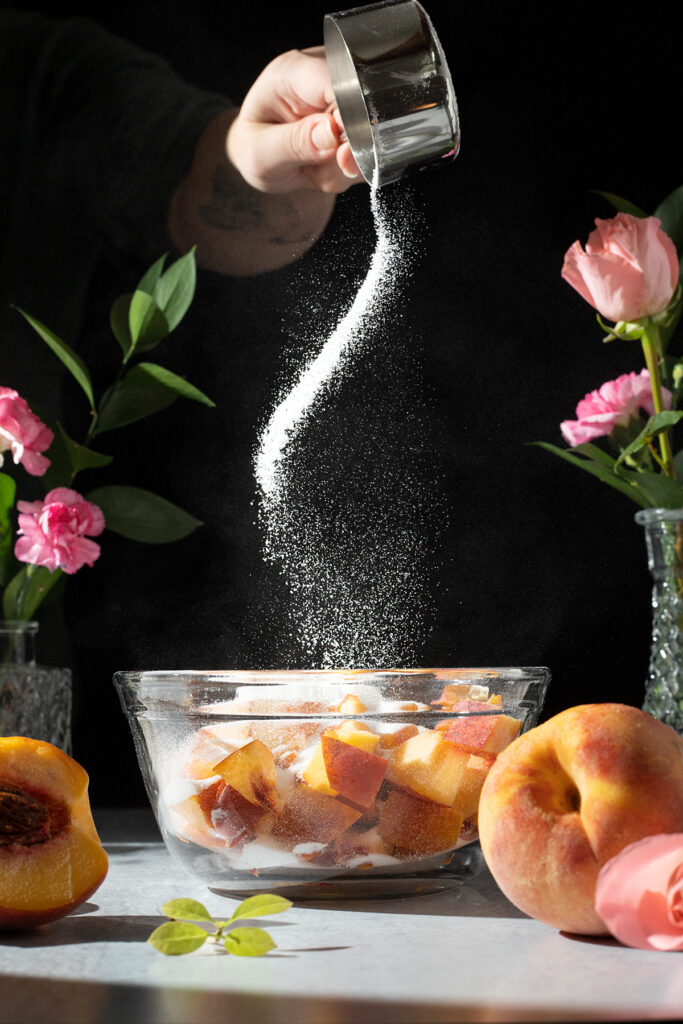 sprinkling sugar onto peaches in a bowl.
