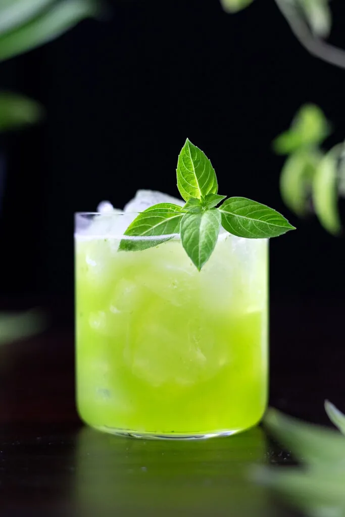 green basil smash in a rocks glass with basil leaves.