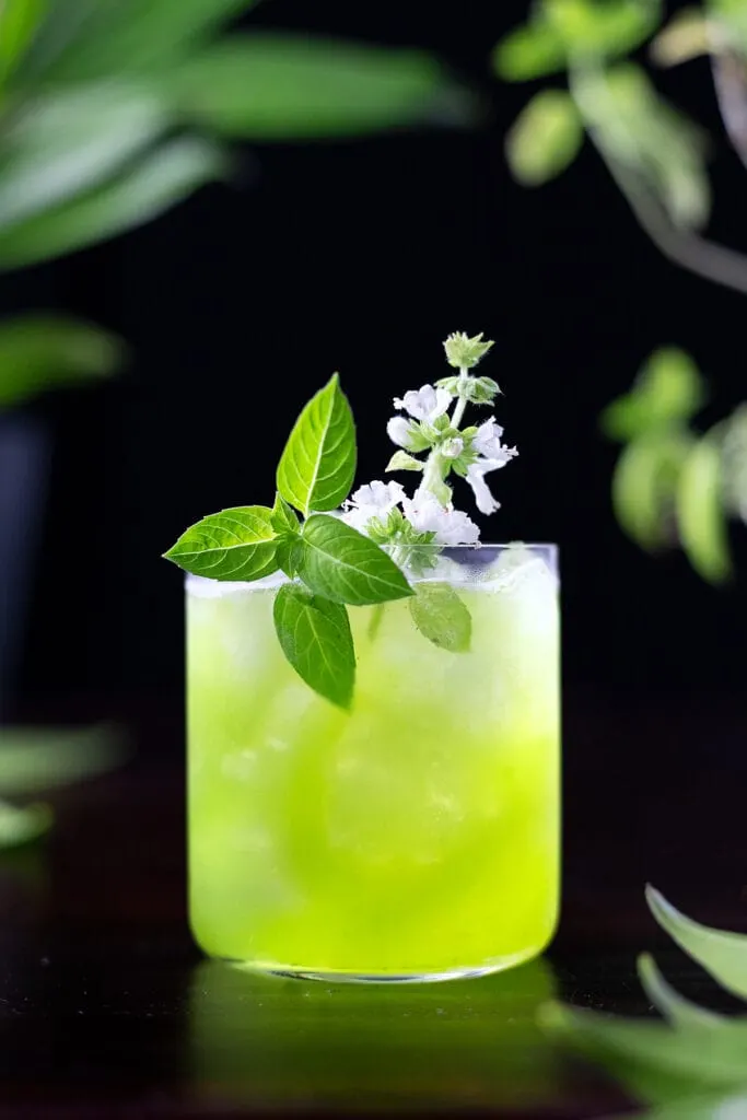 green basil smash in a rocks glass with basil leaves and a basil flower.