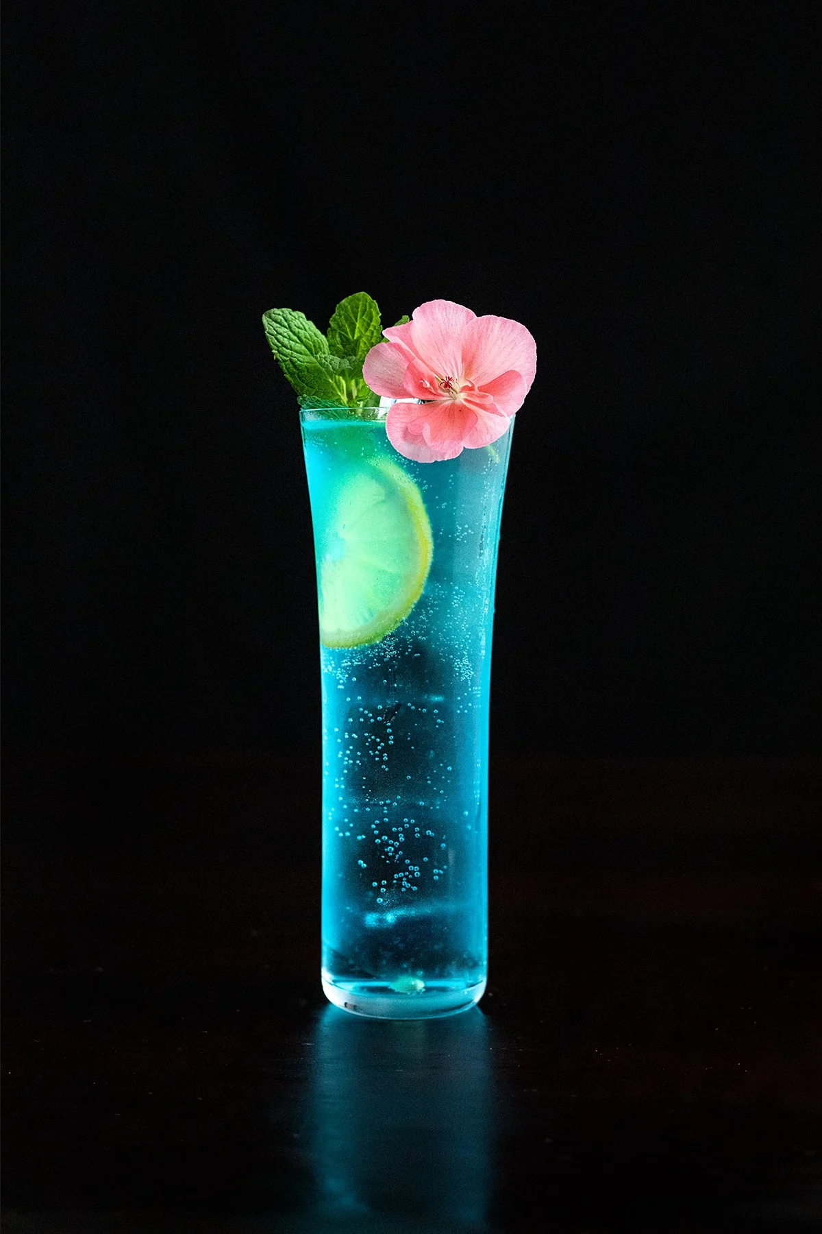 tall blue cocktail with mint and a pink flower.