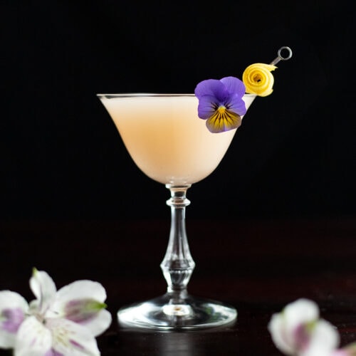 a pale creamy cocktail garnished with edible flowers.