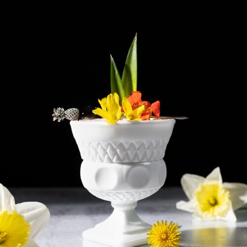 tropical cocktail in a white glass cup with flowers and pineapple leaves.