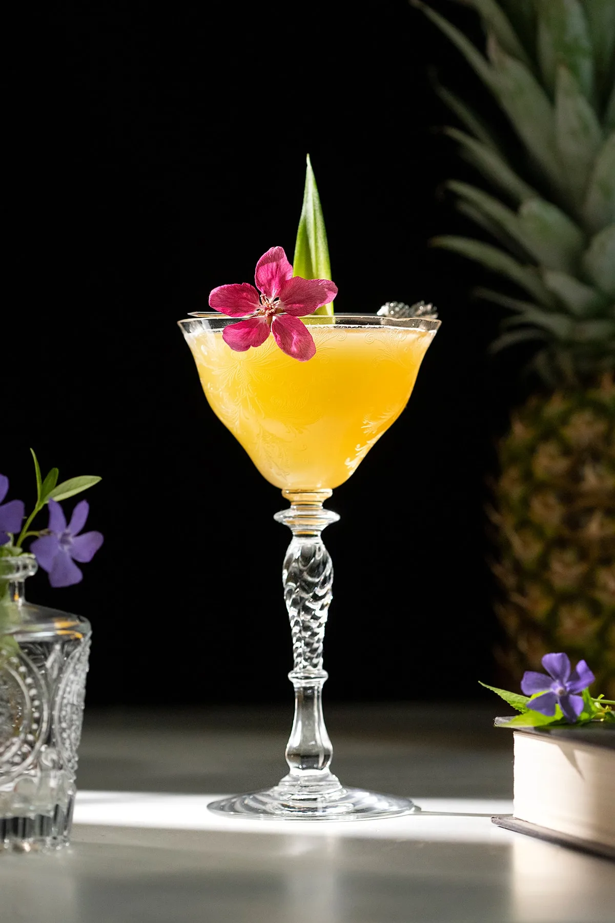 yellow cocktail with a flower and pineapple leaf