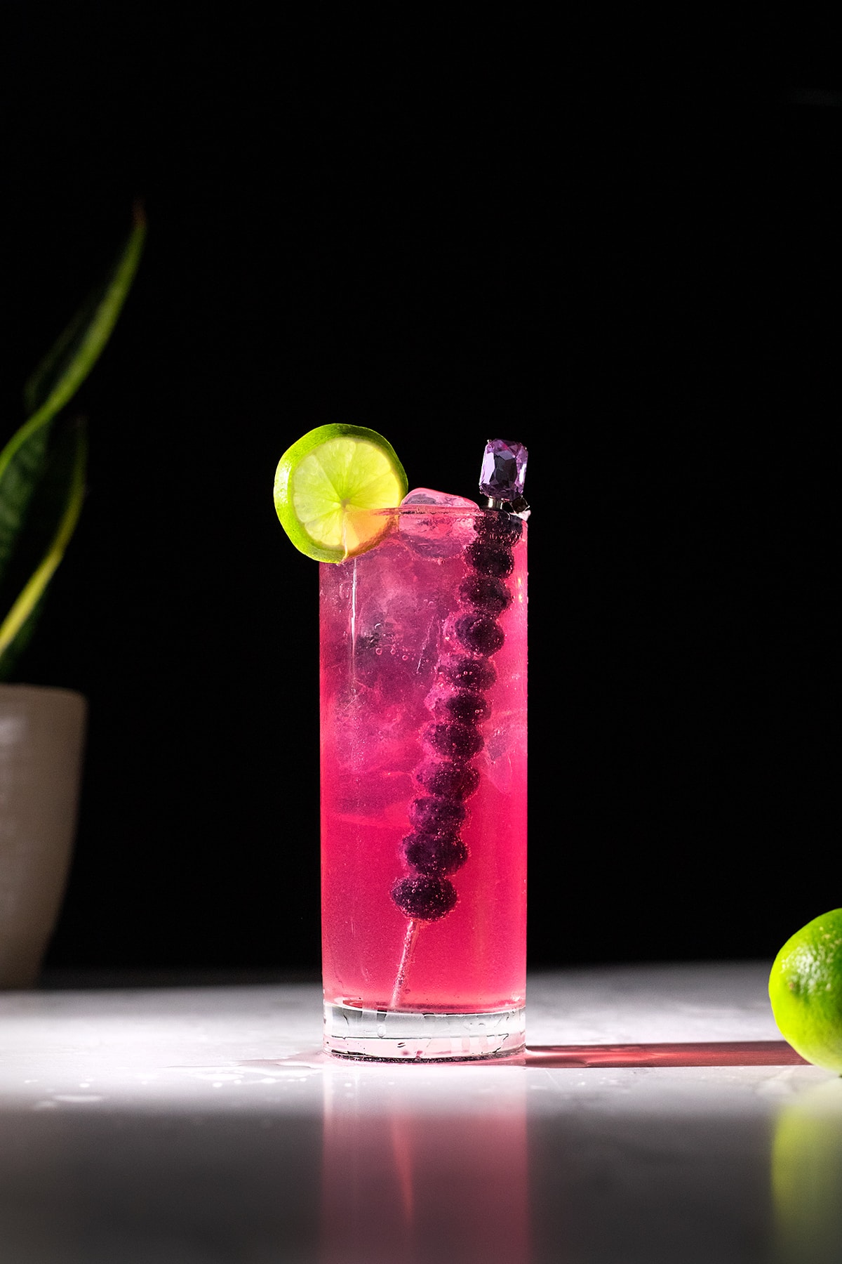 a bright pink highball cockail with a lime wheel