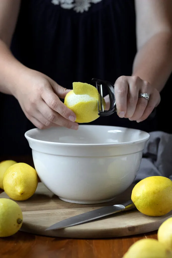 hands peeling lemons over a mixing bowl.