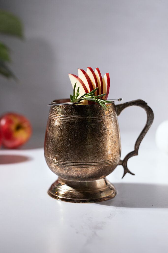 close up of a tarnished mule mug with an apple fan and rosemary sprig.