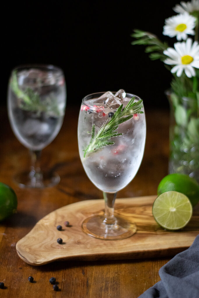 a goblet filled with a clear, bubbly drink, rosemary and pink peppercorns.