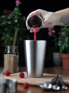 pouring bright red syrup into a cocktail shaker.