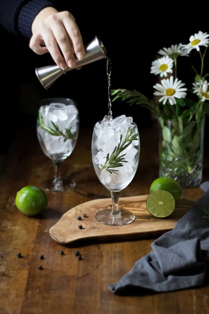 pouring gin from a jigger into a glass full of ice.