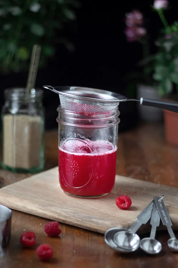 straining raspberry syrup through a fine mesh strainer into a mason jar